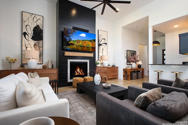 living room featuring wood-type flooring, a large fireplace, and ceiling fan