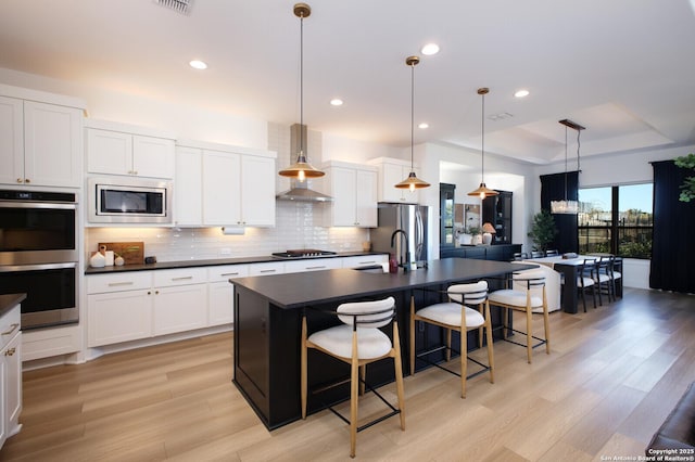 kitchen with appliances with stainless steel finishes, a center island with sink, white cabinets, and decorative light fixtures