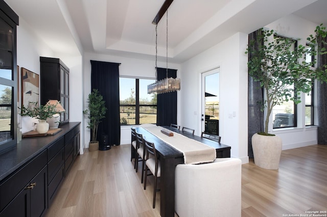 dining space featuring a raised ceiling, an inviting chandelier, and light wood-type flooring