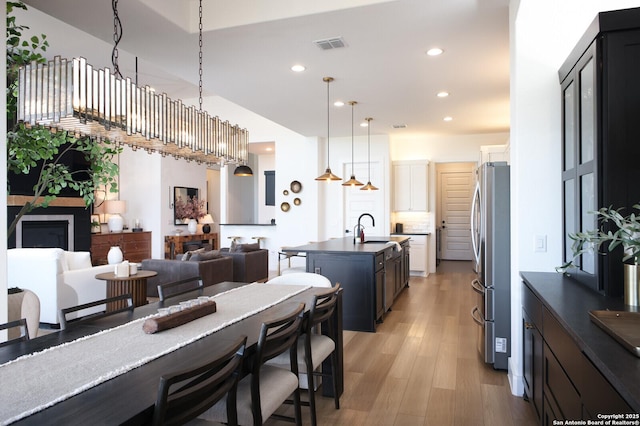 kitchen with sink, light wood-type flooring, stainless steel fridge, an island with sink, and pendant lighting