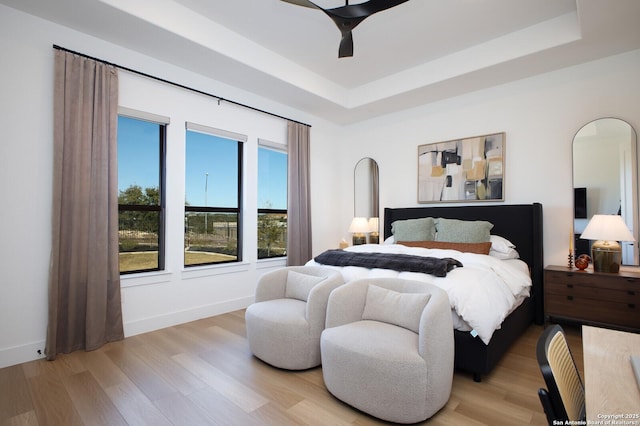 bedroom with light hardwood / wood-style floors, a raised ceiling, and ceiling fan