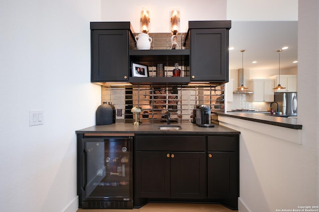 bar with wall chimney range hood, sink, stainless steel refrigerator, backsplash, and wine cooler