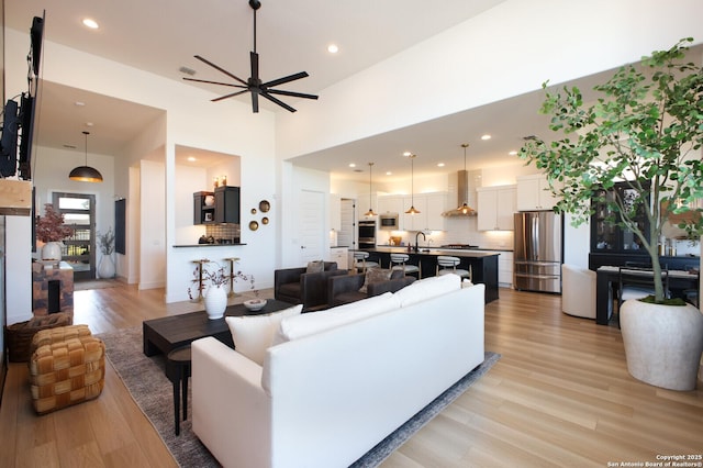 living room with ceiling fan, sink, light hardwood / wood-style flooring, and a towering ceiling