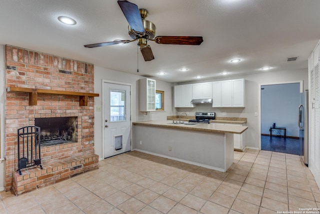 kitchen with a fireplace, white cabinets, light tile patterned floors, kitchen peninsula, and stainless steel appliances