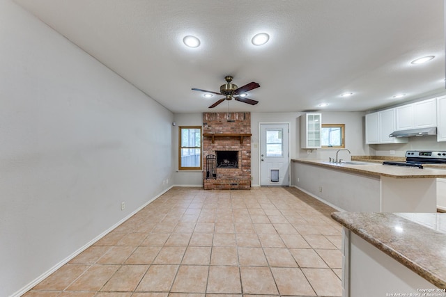 unfurnished living room featuring light tile patterned floors, sink, ceiling fan, a fireplace, and a textured ceiling