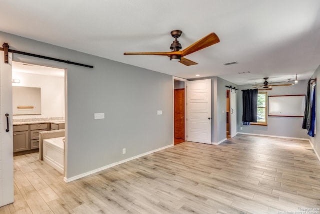 empty room featuring ceiling fan, a barn door, and light hardwood / wood-style floors