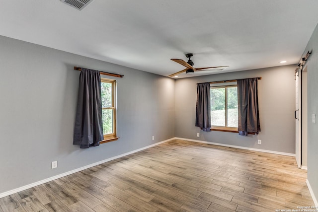 unfurnished room with ceiling fan, a healthy amount of sunlight, a barn door, and light wood-type flooring