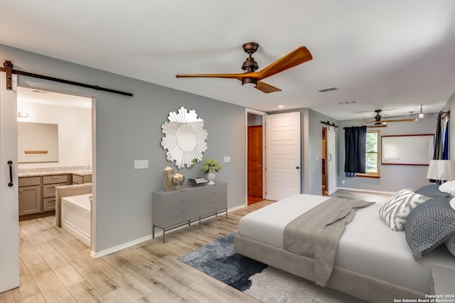 bedroom featuring ceiling fan, ensuite bathroom, a barn door, and light hardwood / wood-style flooring