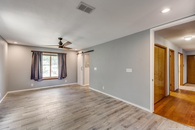 spare room featuring light hardwood / wood-style flooring, a barn door, and ceiling fan