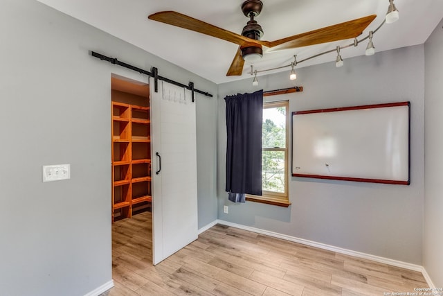 spare room featuring light hardwood / wood-style flooring, a barn door, and ceiling fan