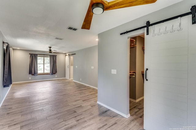 spare room with a barn door, light wood-type flooring, and ceiling fan