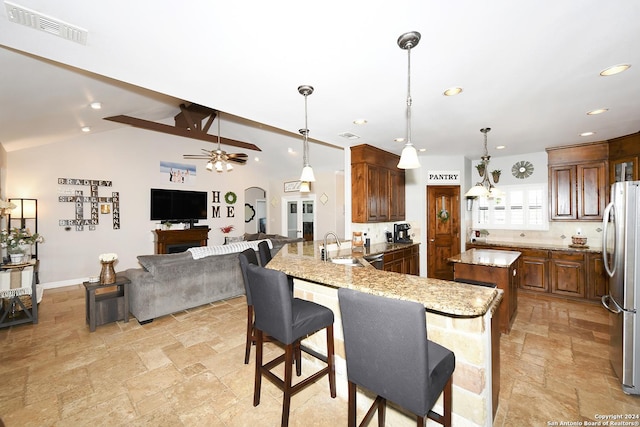 kitchen with stainless steel refrigerator, decorative light fixtures, sink, light stone counters, and kitchen peninsula