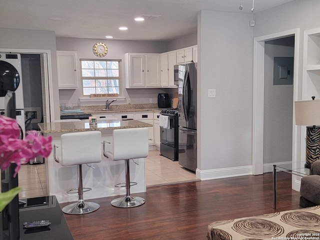 kitchen featuring a breakfast bar, white cabinets, electric panel, light stone countertops, and black appliances