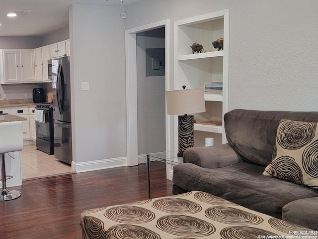 living room featuring built in shelves, light wood-style flooring, and baseboards