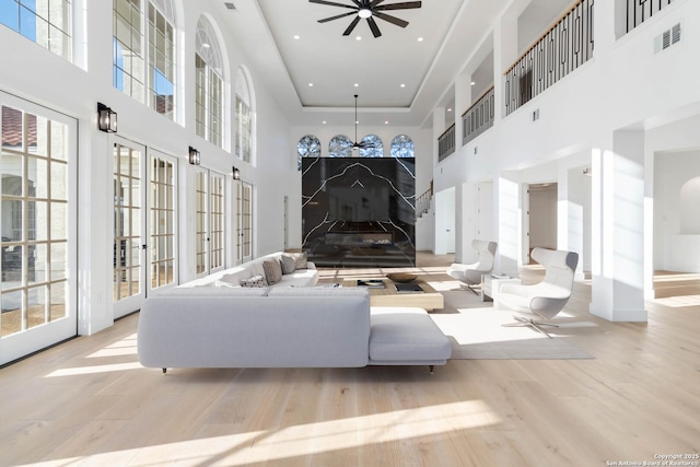 living room with a tray ceiling, light hardwood / wood-style flooring, ceiling fan, and a high ceiling