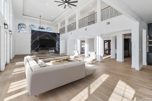 living room with ceiling fan, a tray ceiling, light hardwood / wood-style floors, and a towering ceiling