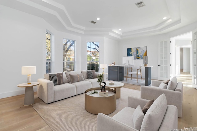 living room with a raised ceiling and light wood-type flooring