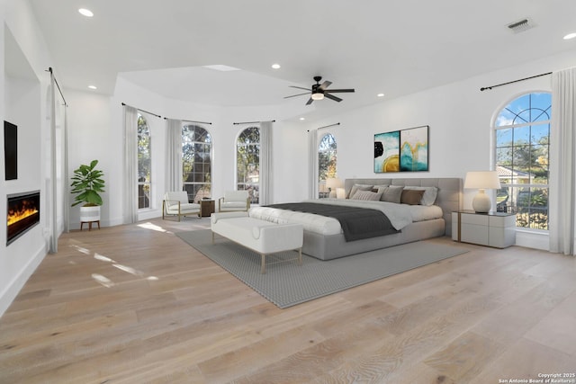 bedroom with access to outside, a large fireplace, ceiling fan, and light wood-type flooring