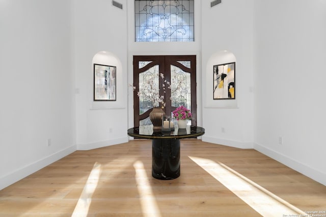 entrance foyer with french doors, wood-type flooring, and a high ceiling