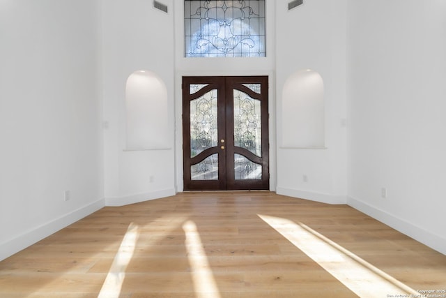 entrance foyer with a towering ceiling, french doors, and light wood-type flooring