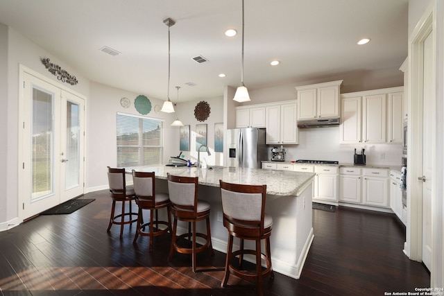 kitchen featuring french doors, white cabinetry, hanging light fixtures, stainless steel appliances, and a kitchen island with sink