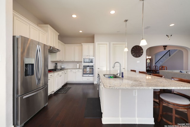 kitchen featuring sink, light stone counters, decorative light fixtures, appliances with stainless steel finishes, and a kitchen island with sink