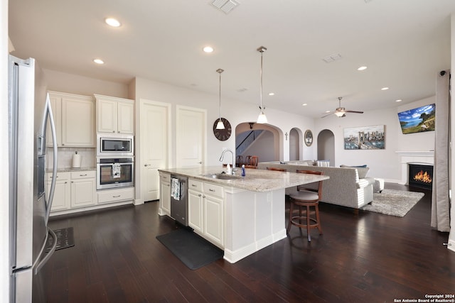 kitchen featuring sink, decorative light fixtures, stainless steel appliances, light stone countertops, and a kitchen island with sink