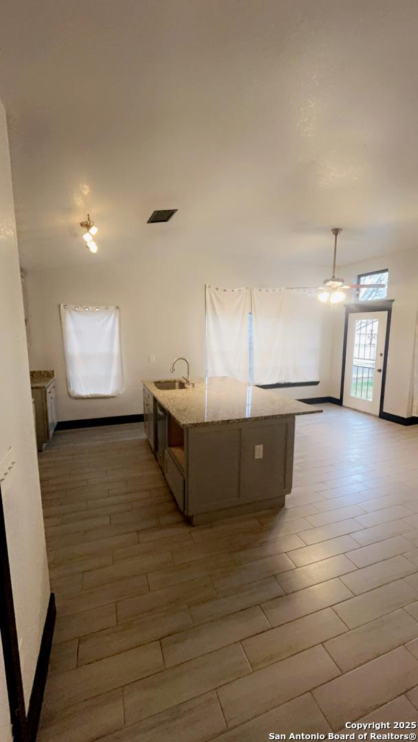 kitchen featuring sink, ceiling fan, light hardwood / wood-style floors, light stone countertops, and a center island with sink