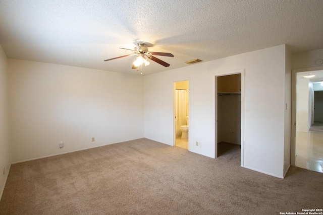 unfurnished bedroom featuring a walk in closet, ceiling fan, carpet, and a textured ceiling