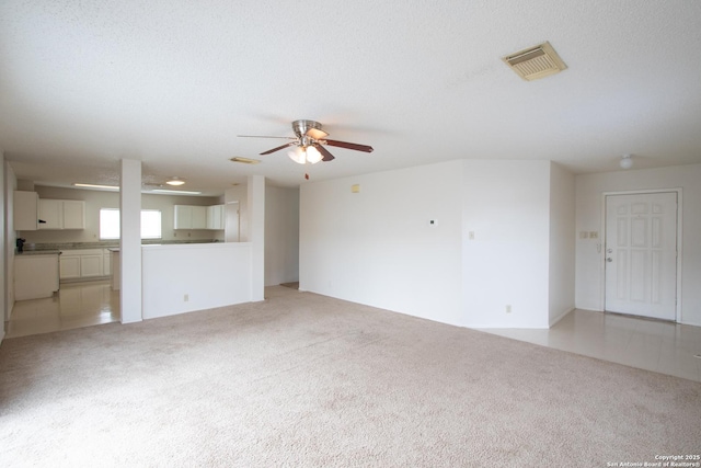 unfurnished living room featuring ceiling fan, light colored carpet, and a textured ceiling