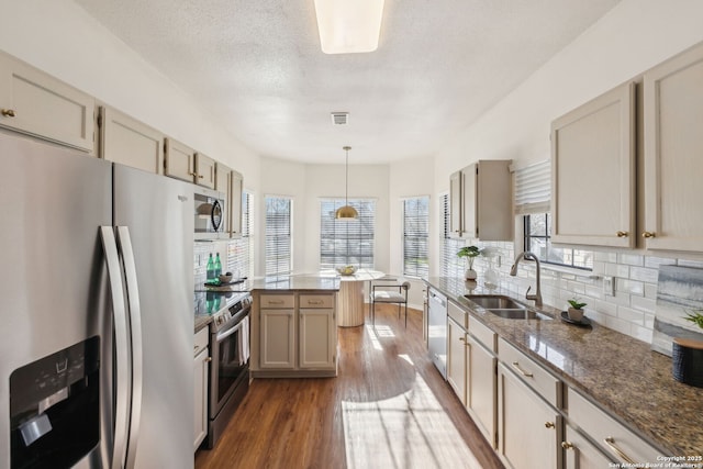 kitchen featuring appliances with stainless steel finishes, sink, hanging light fixtures, light stone counters, and dark wood-type flooring