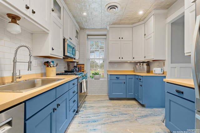 kitchen with white cabinetry, blue cabinetry, appliances with stainless steel finishes, and sink