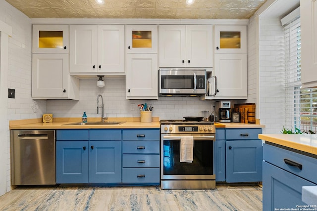 kitchen with sink, blue cabinetry, stainless steel appliances, white cabinets, and decorative backsplash