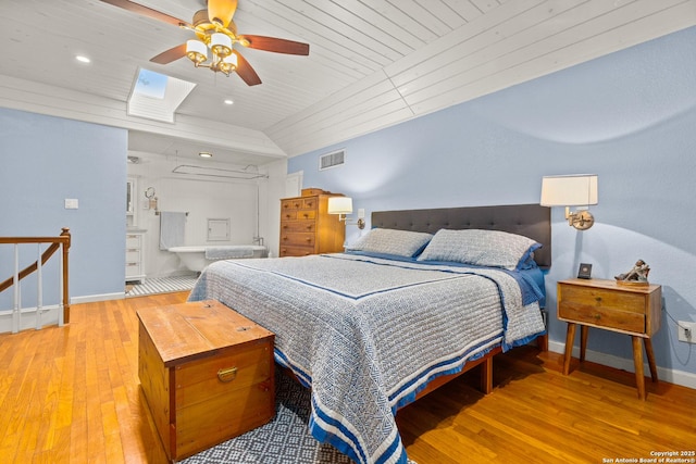 bedroom with hardwood / wood-style flooring, ensuite bath, vaulted ceiling with skylight, and ceiling fan