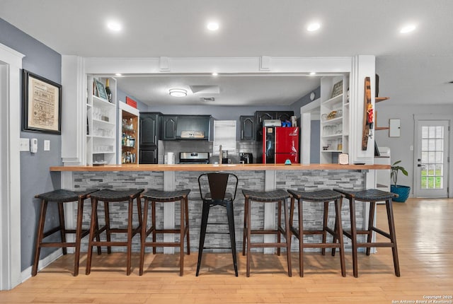 bar featuring fridge, backsplash, stainless steel electric stove, and light wood-type flooring