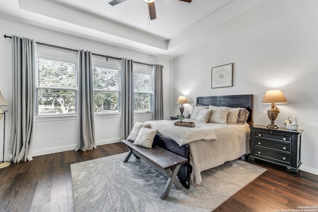 bedroom with ceiling fan, dark hardwood / wood-style floors, and a raised ceiling