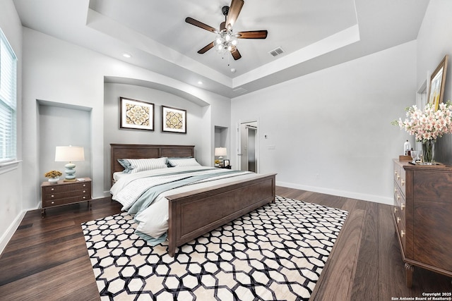 bedroom featuring a raised ceiling, dark wood-type flooring, and ceiling fan