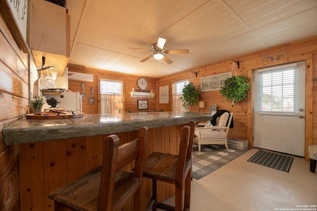 kitchen with ceiling fan, a healthy amount of sunlight, wooden walls, and kitchen peninsula