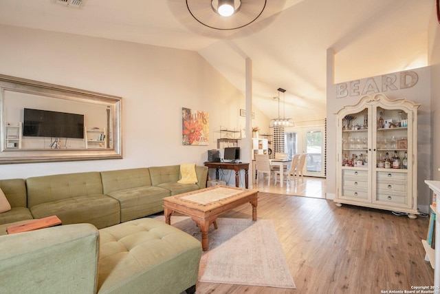 living room with an inviting chandelier, vaulted ceiling, and light wood-type flooring