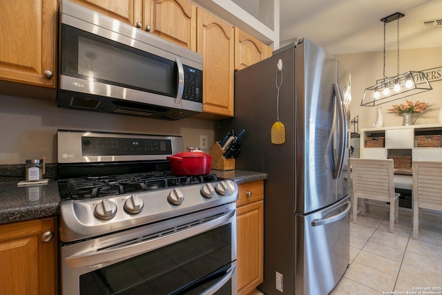 kitchen with light tile patterned flooring, appliances with stainless steel finishes, pendant lighting, and dark stone countertops