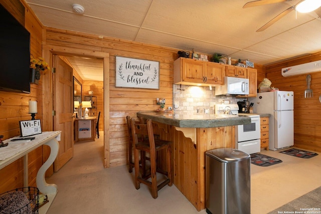 kitchen with light brown cabinetry, wood walls, a breakfast bar area, ceiling fan, and white appliances