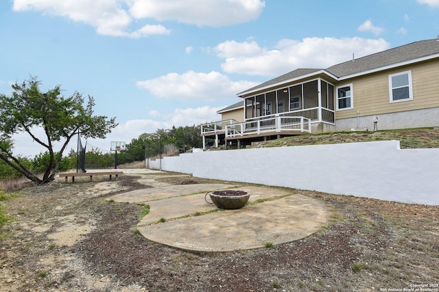 back of property featuring a wooden deck, a sunroom, a patio, and a fire pit