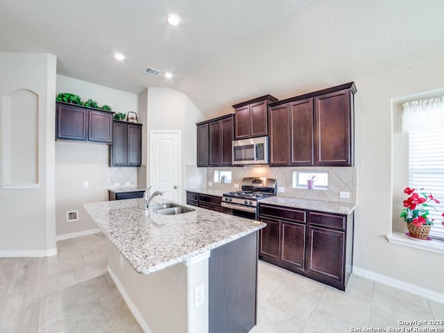 kitchen featuring sink, appliances with stainless steel finishes, light stone counters, a center island with sink, and decorative backsplash