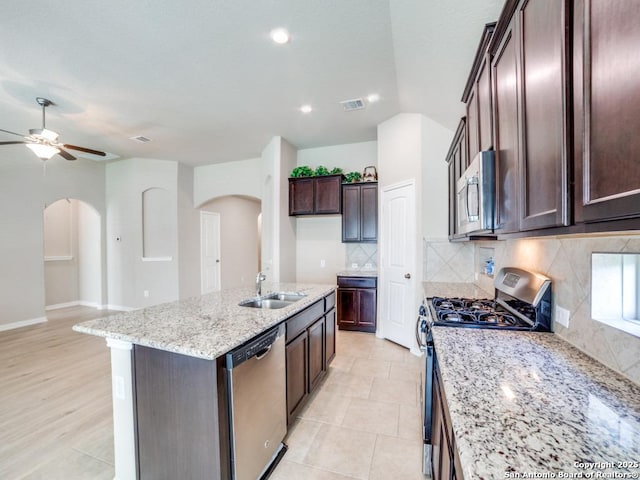 kitchen with sink, a center island with sink, appliances with stainless steel finishes, light stone countertops, and backsplash