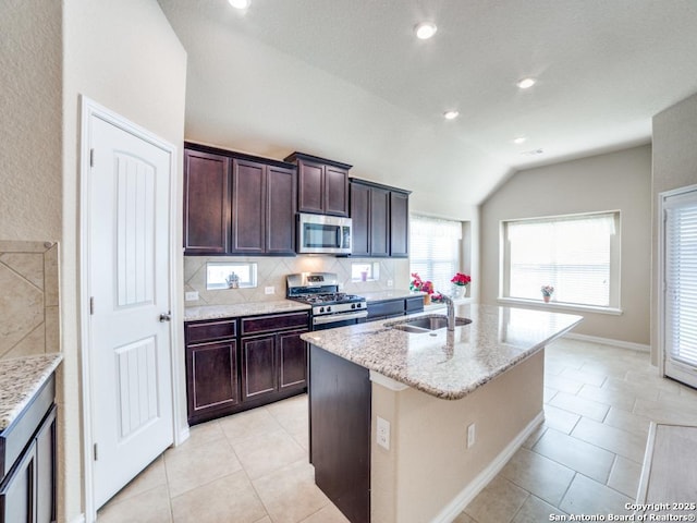 kitchen featuring vaulted ceiling, appliances with stainless steel finishes, an island with sink, sink, and light stone counters