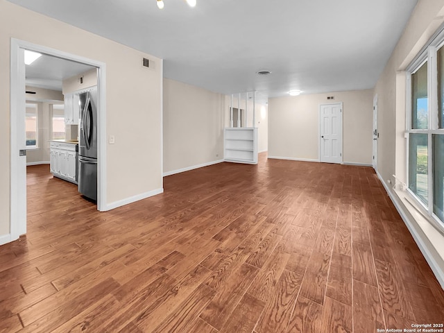 unfurnished living room featuring plenty of natural light, wood finished floors, visible vents, and baseboards