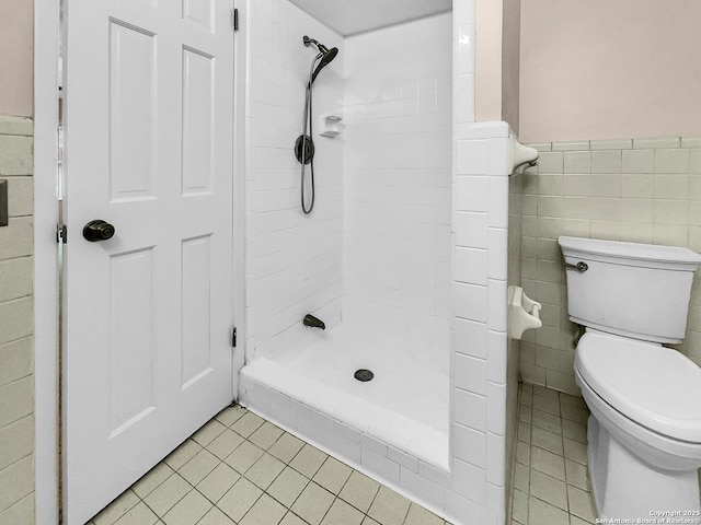 bathroom with tiled shower, tile patterned floors, toilet, and tile walls