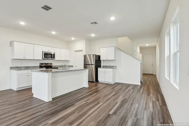 kitchen featuring white cabinetry, stainless steel appliances, light stone countertops, and an island with sink