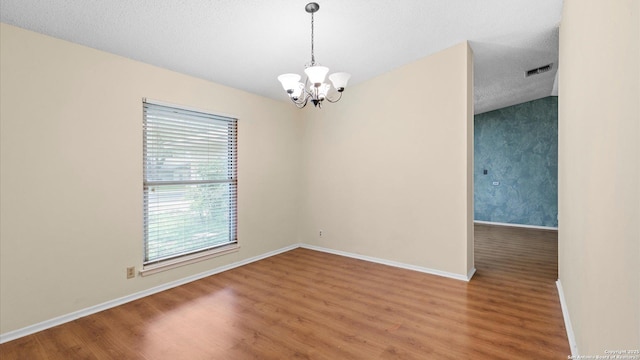 empty room featuring an inviting chandelier, wood-type flooring, and a textured ceiling