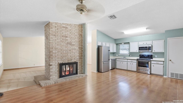 kitchen featuring appliances with stainless steel finishes, a fireplace, white cabinetry, lofted ceiling, and a textured ceiling